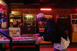 Teenager joyfully playing pinball in a nostalgic retro arcade setting.